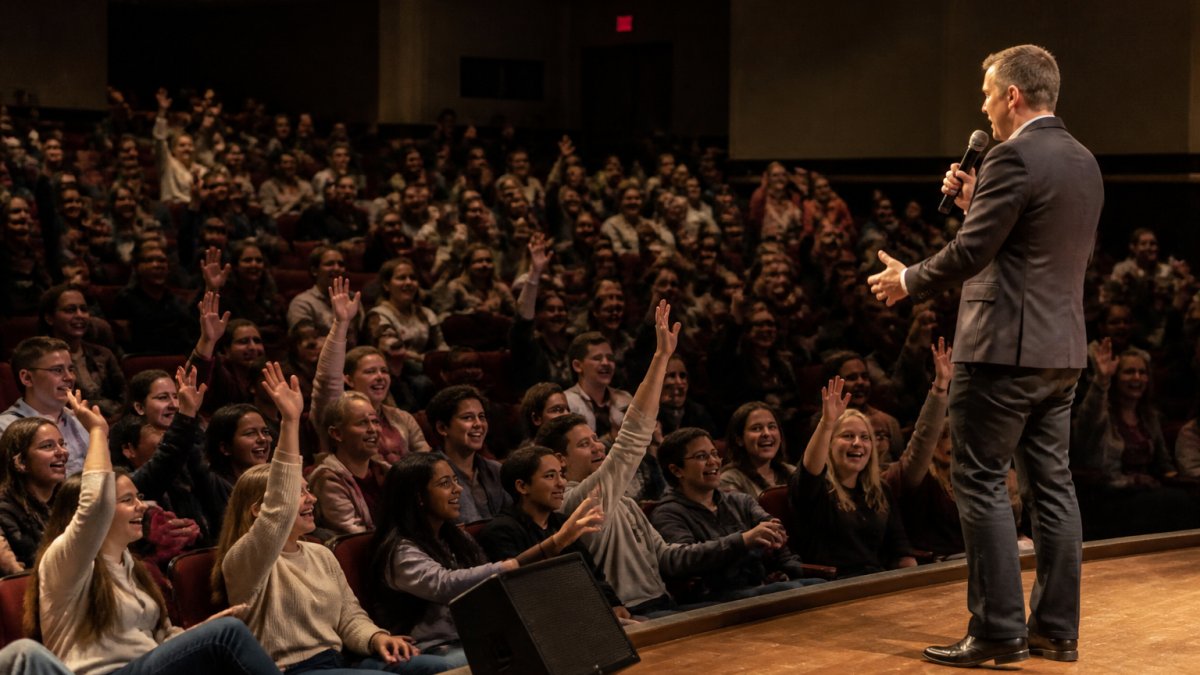 A stage hypnotist performs for an enthusiastic crowd of students in a college auditorium.